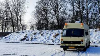 Bassie, een crèmekleurige Volkswagen LT28, op een besneeuwde parkeerplaats tussen kale bomen
