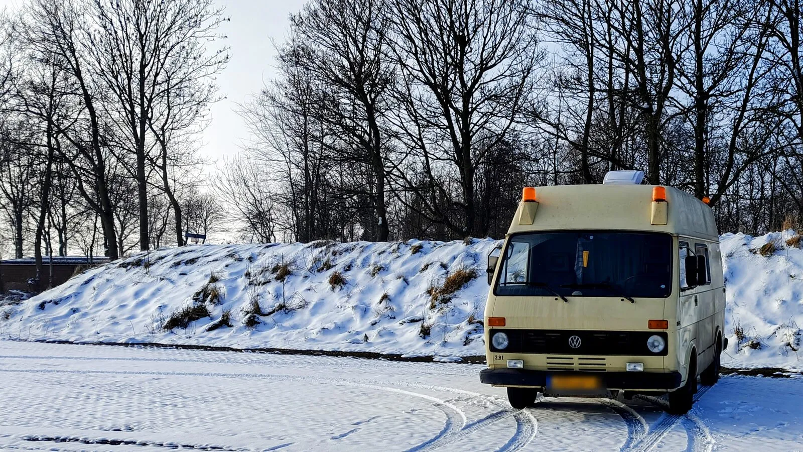 Bassie, een crèmekleurige Volkswagen LT28, op een besneeuwde parkeerplaats tussen kale bomen