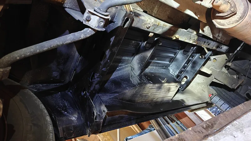 De onderkant van de bus, vers zwart gespoten met bitumen-undercoating