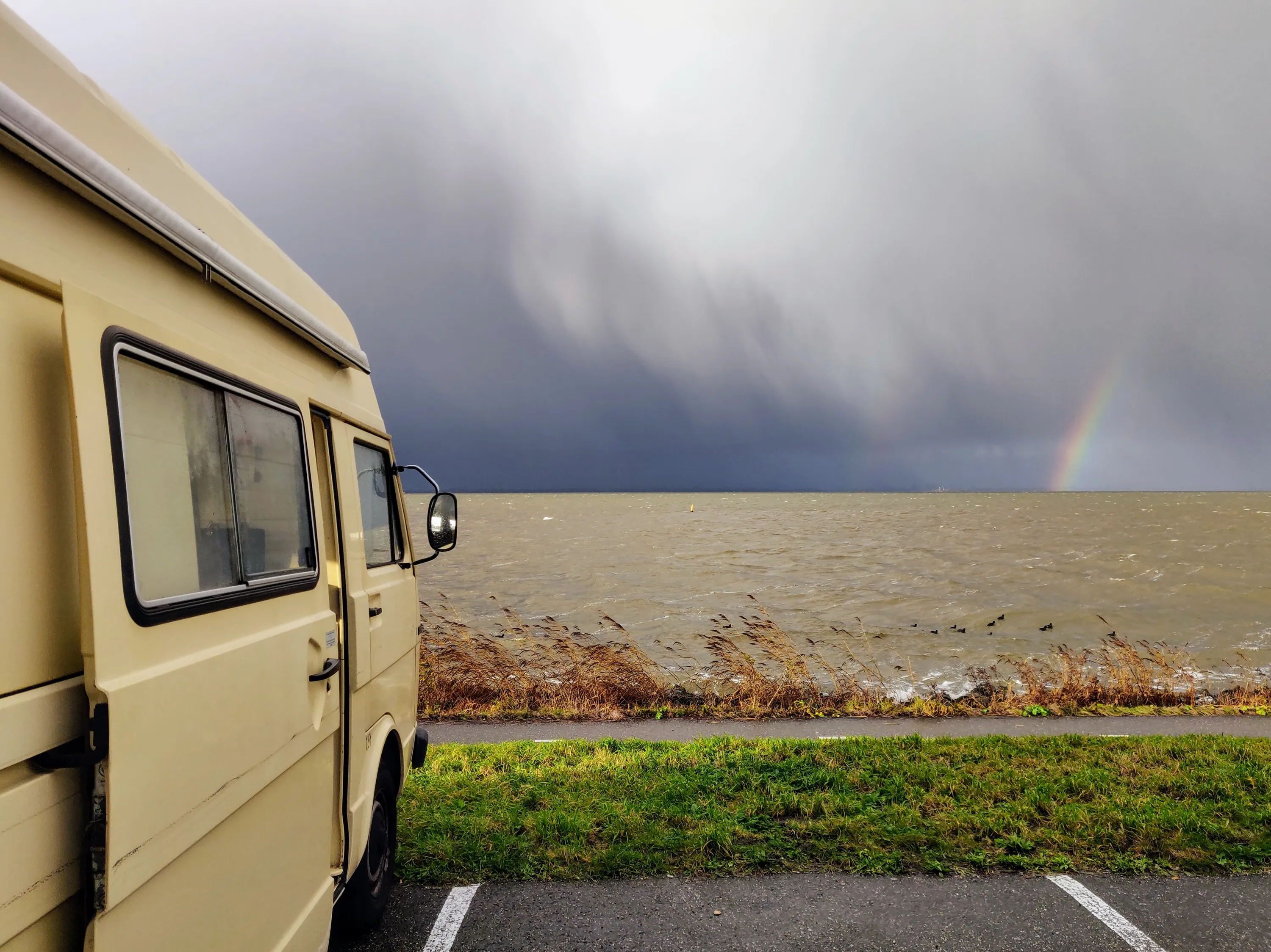 Bassie, mijn Volkswagen LT28, geparkeerd aan het water met donkere wolken en een regenboog